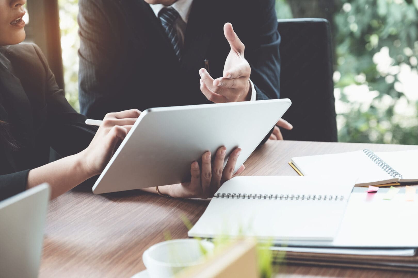 Two people in business attire discuss medical record chronology services around a tablet at a wooden table, surrounded by notebooks and documents.
