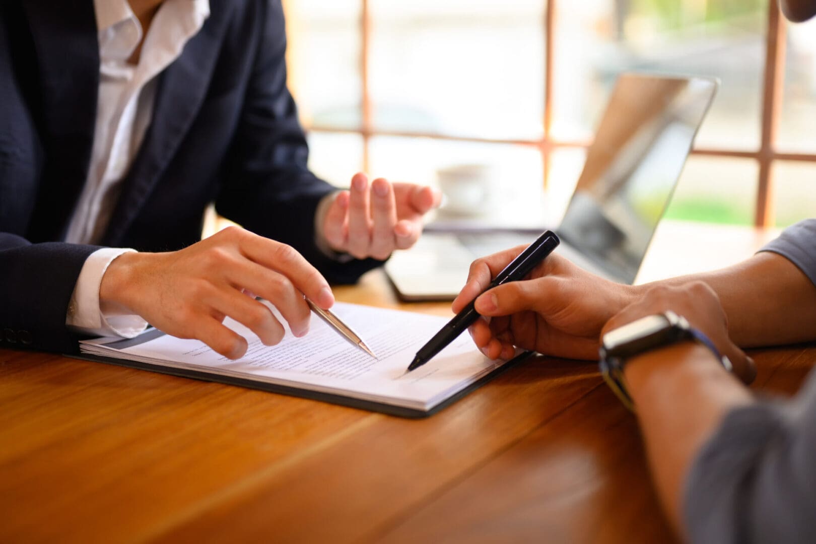 Closeup lawyer or insurance agent pointing at contract showing male client where to signature sign Two people discussing a document at a wooden table, one pointing with a pen.
