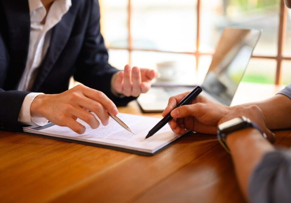 Two people discussing a document at a wooden table, one pointing with a pen.